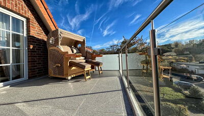 Blick auf einen Balkonboden, rechts ist eine Edelstahlgeländer zu sehen mit Glasfüllung und dem Blick in den Himmel